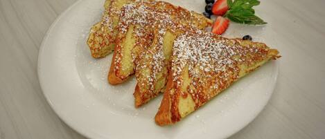A plate with three triangular pastries dusted with powdered sugar, accompanied by strawberries and blueberries.