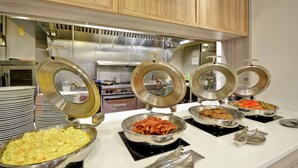 A buffet setup with various food items in bowls, a stove, and stacked plates. - Hilton Garden Inn Ridgefield Park (Ridgefield Park)