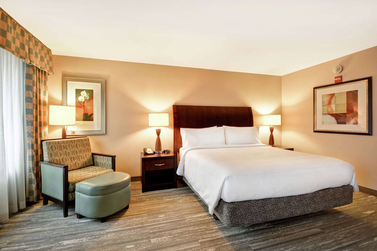 A hotel room with a bed, a chair, a nightstand, and a lamp.