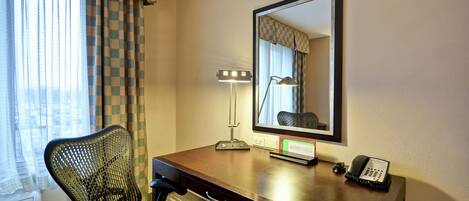 Ett hotellrum med ett skrivbord, en stol, en lampa, en telefon och en stor spegel.