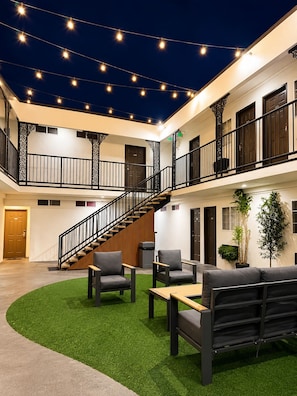 A multi-level atrium with a central staircase, seating area with sofas and tables, and string lights. - The Beverly House by AGA - Beverly Hills (Los Angeles)