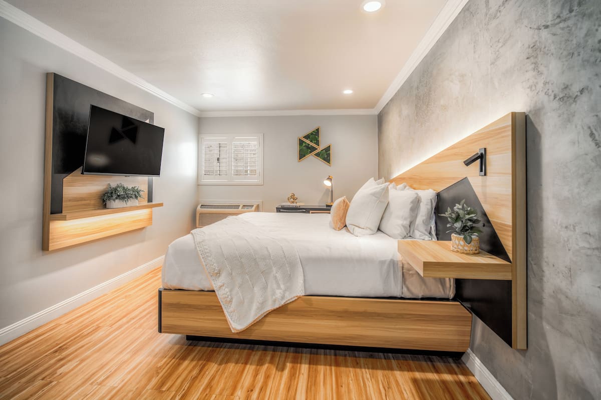A modern bedroom with a bed, TV, wooden headboard, and a wall-mounted shelf.