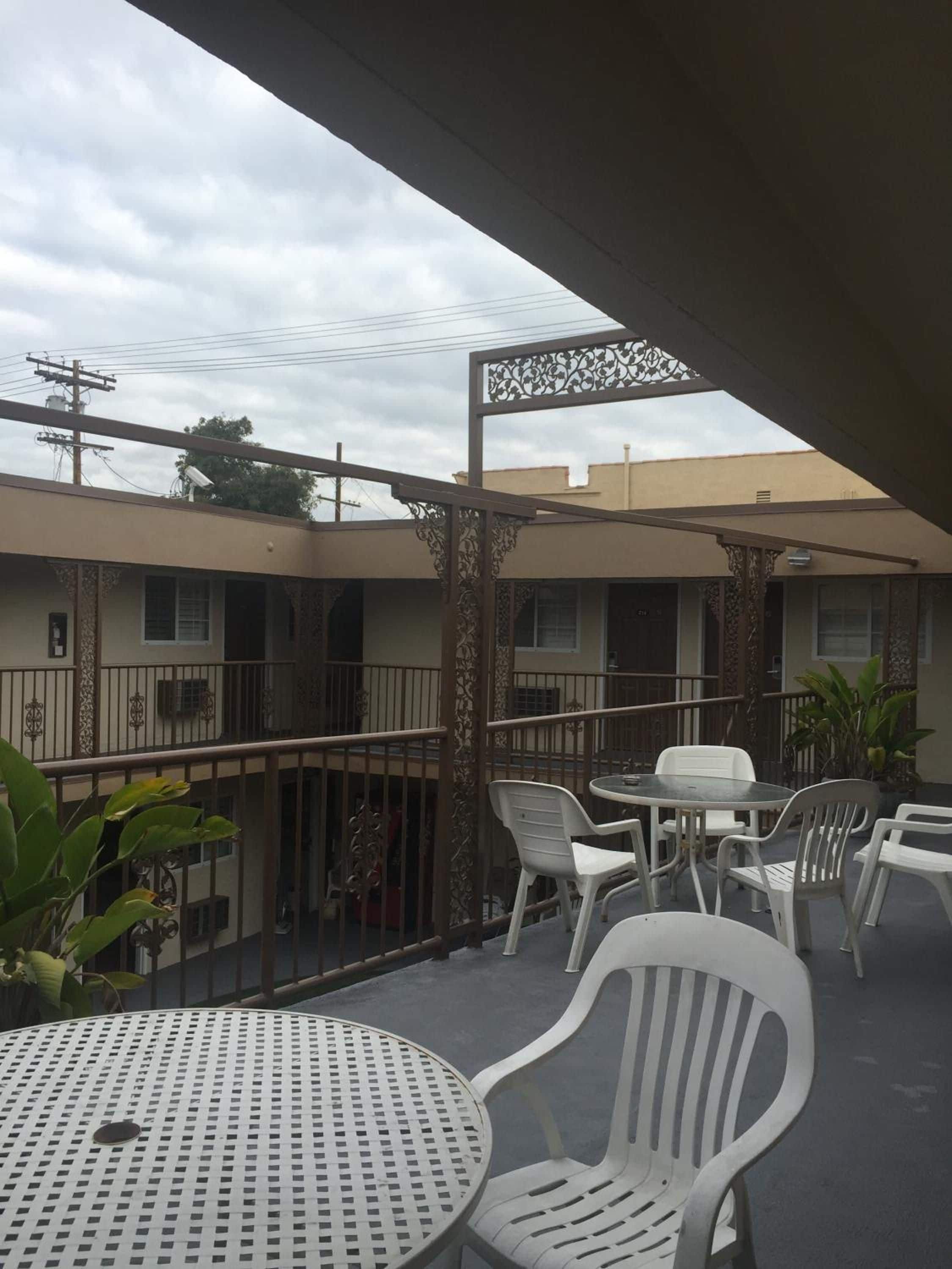 A covered outdoor area with a round table and chairs, a decorative metal fence, and a building with multiple windows in the background.