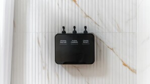 A black, rectangular device with three knobs labeled 'Refreshing Body Wash,' 'Soothing Conditioner,' and 'Cleansing Shampoo' on a white, ribbed surface. - The Beverly House by AGA - Beverly Hills (Los Angeles)