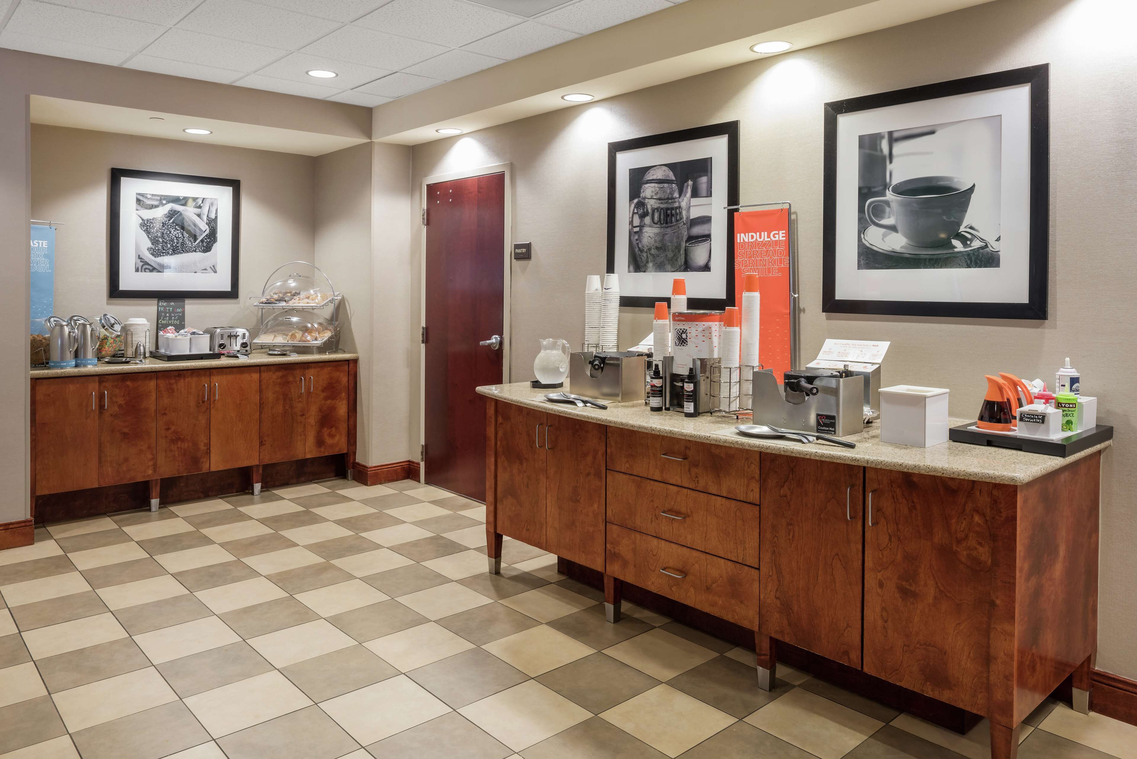 A hotel reception area with a checkered floor, wooden cabinets, a coffee station, and framed pictures on the walls.