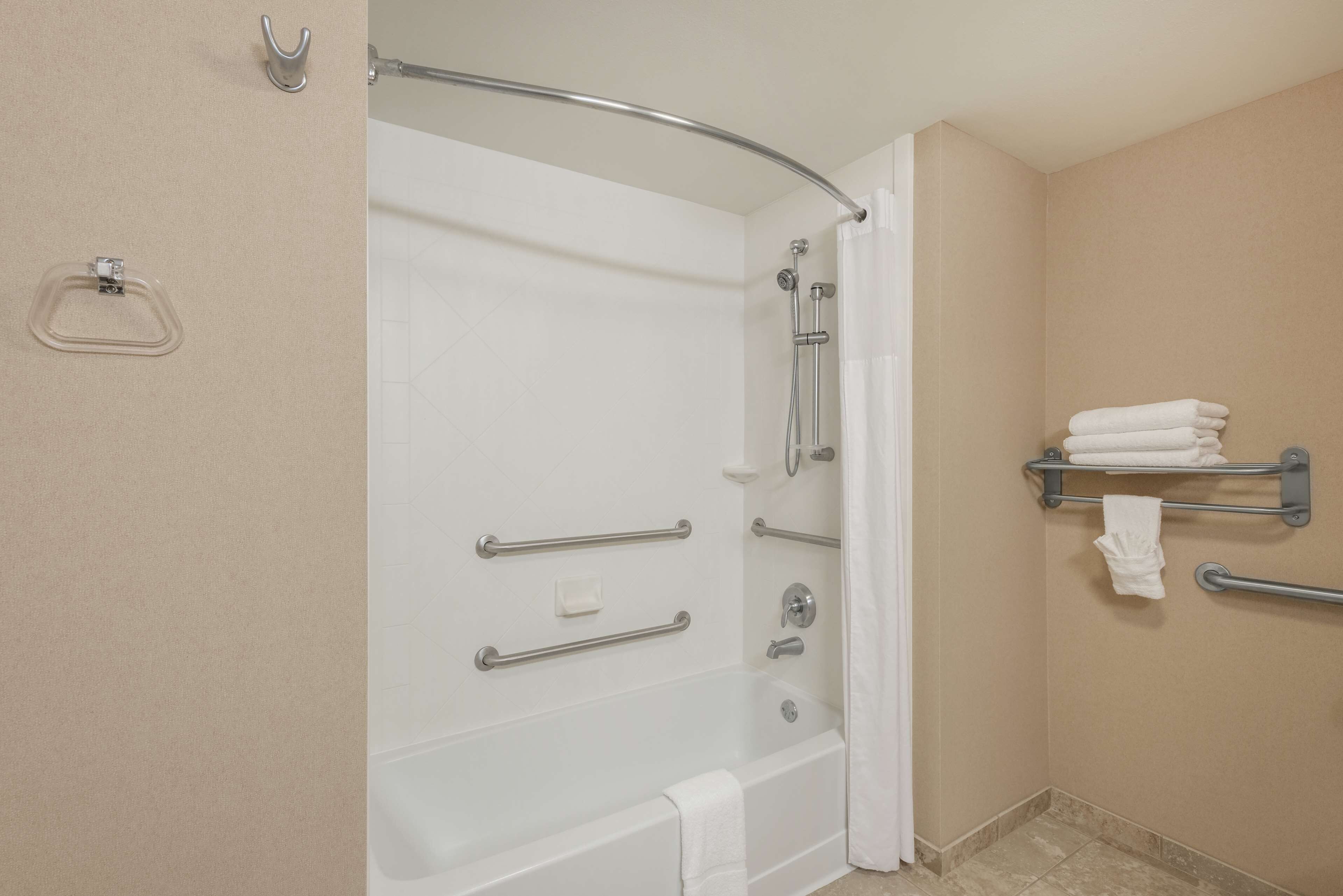 A bathroom with a bathtub, grab bars, a towel rack, and a shower curtain.