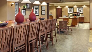 Un comedor con sillas de madera y una mesa, una zona de bar con mostrador y taburetes, y cuadros en las paredes.