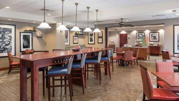 A hotel dining area with wooden tables and chairs, pendant lighting, and framed artwork on the walls.