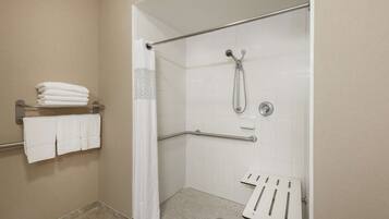 Ducha a ras de suelo con puerta de cristal, barra de apoyo metálica, toallero blanco y panel de control de la ducha.