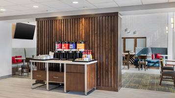 A modern hotel lobby with a coffee station, seating area, and a TV mounted on the wall.