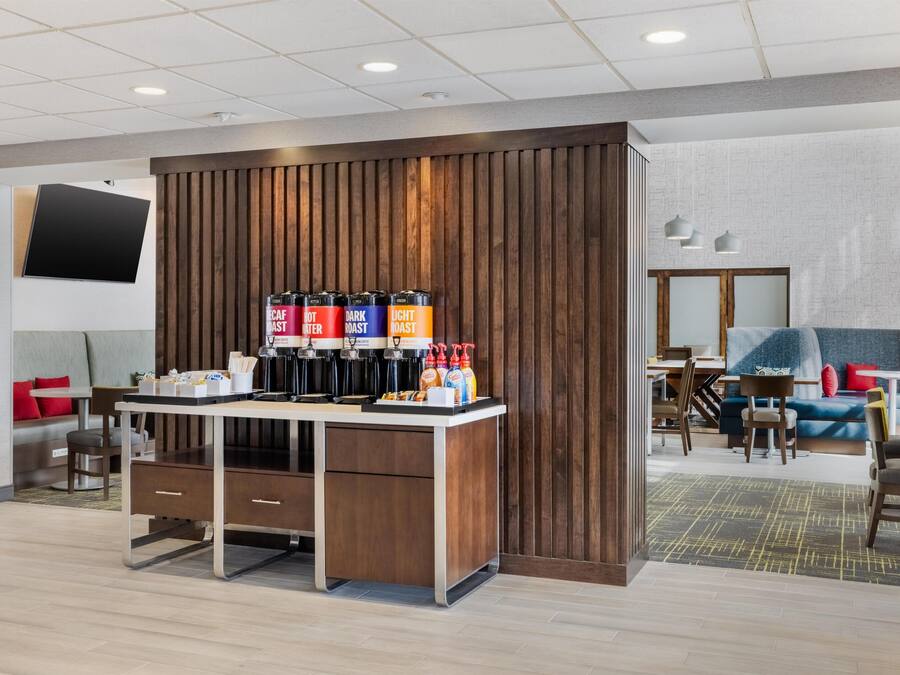 A modern hotel lobby with a coffee station, seating area, and a TV mounted on the wall.