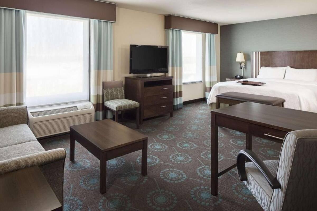 A hotel room with a bed, a TV, a desk, a chair, and a sofa.