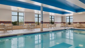 Ein Schwimmbecken mit Liegestühlen und Tischen, großen Fenstern und blauer Decke.