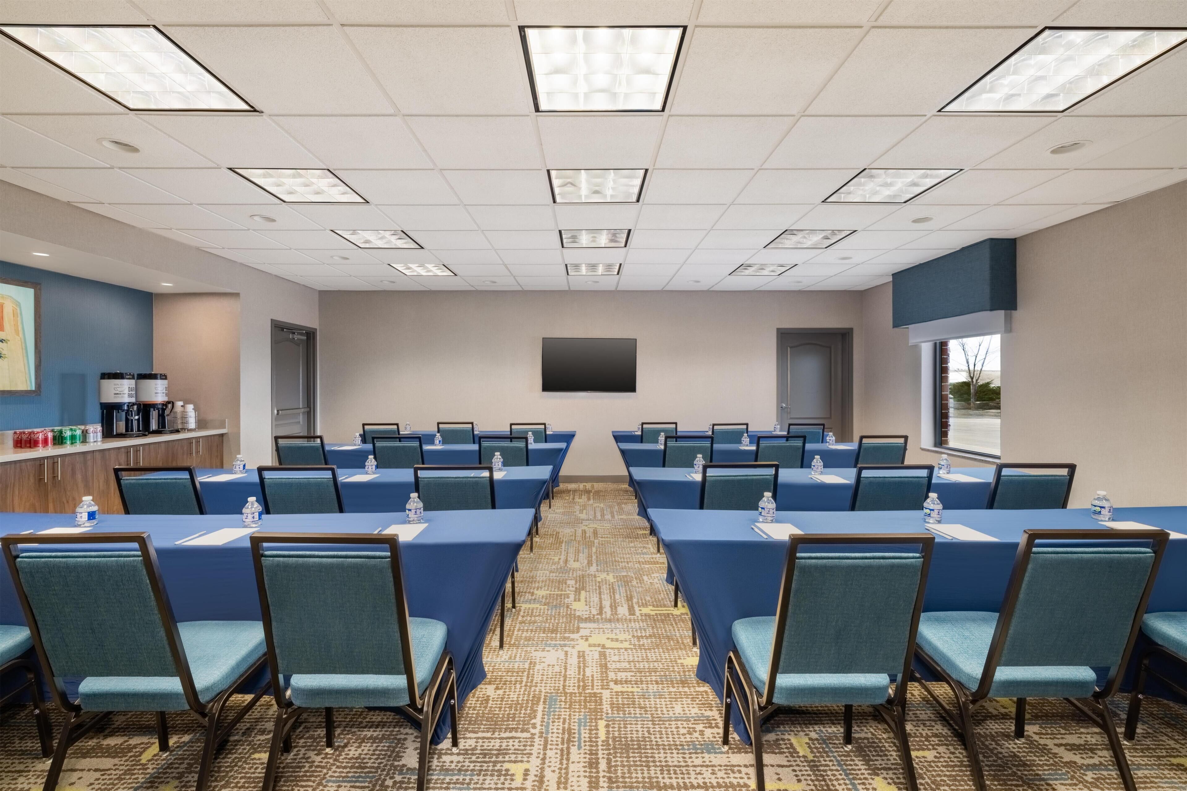 A conference room with tables, chairs, a projector screen, and a window.