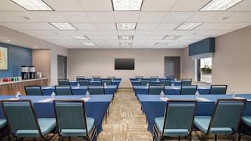 A conference room with tables, chairs, a projector screen, and a window.