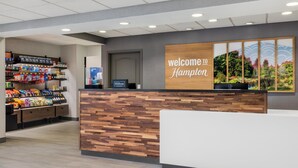 Ein Empfangsschalter mit einem 'Welcome to Hampton'-Schild, einer Auswahl an Snacks und einem 'Hilton Honors'-Schild.