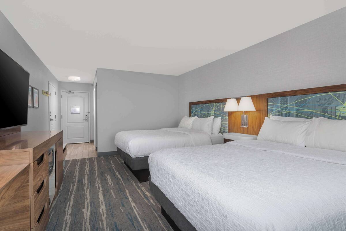 A hotel room with two beds, a desk with a TV, and a bathroom door.
