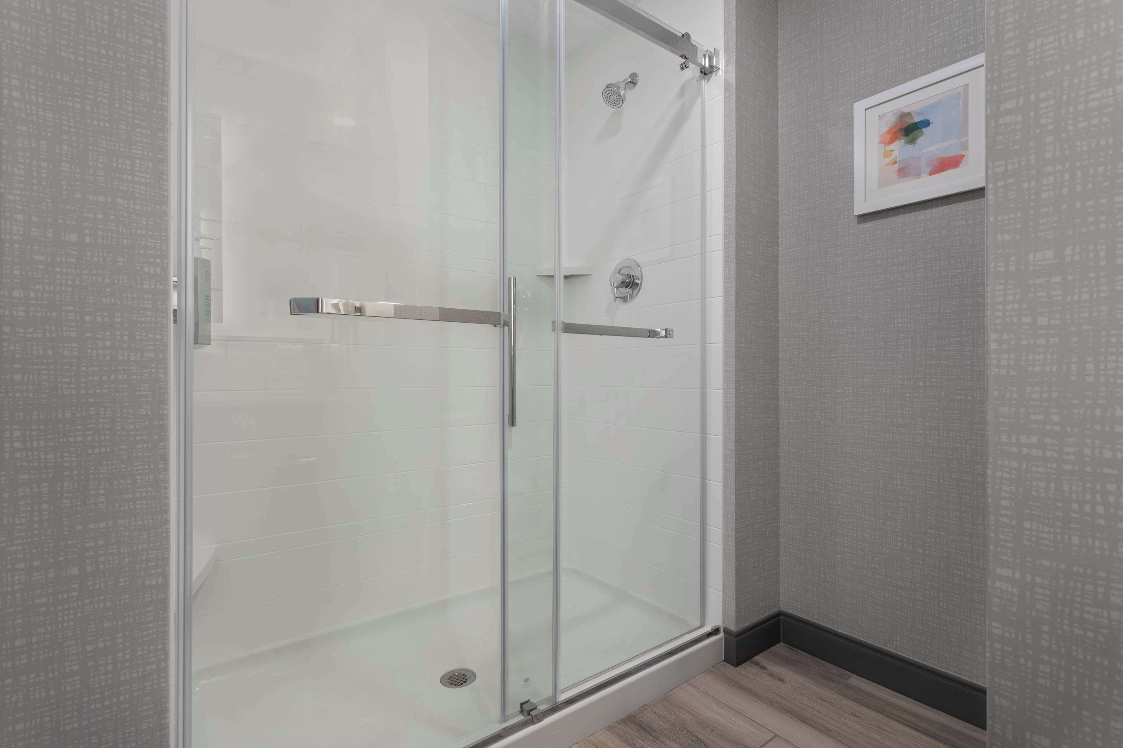 A glass-enclosed shower with a metal handle and a wall-mounted towel rack.