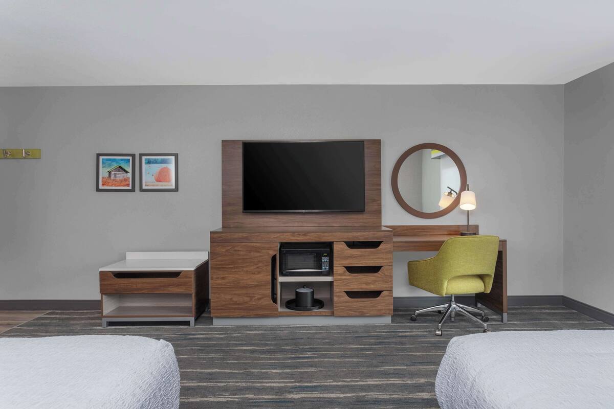 A hotel room with a flat-screen TV, a microwave, a sink, a mirror, and a yellow chair.