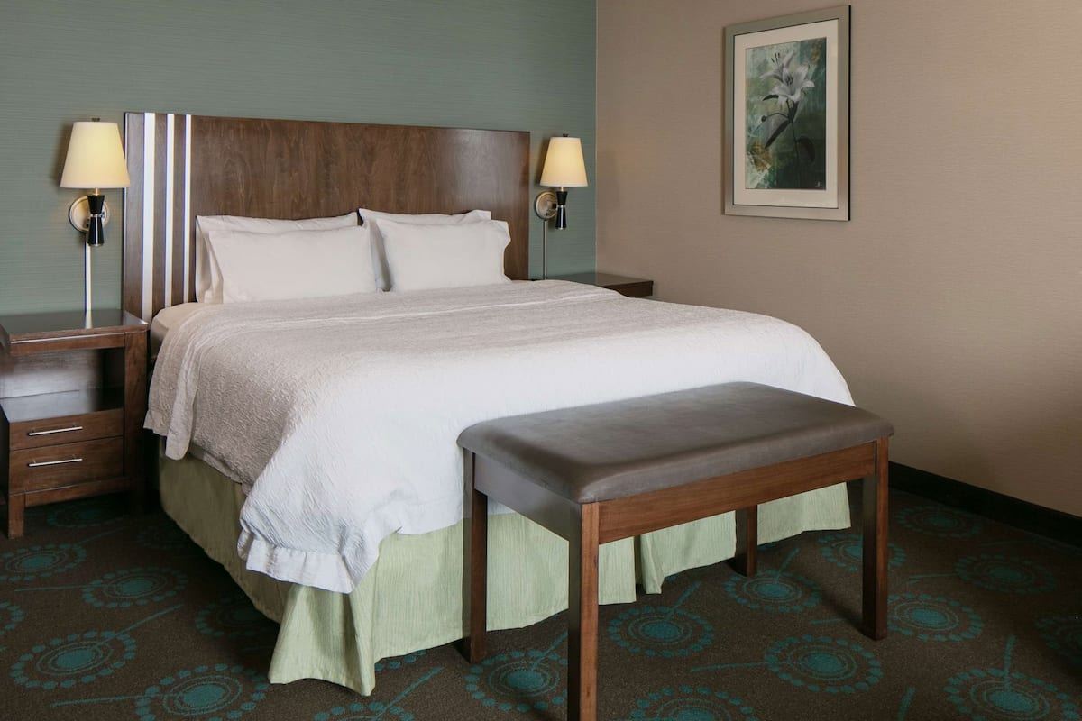 A hotel room with a bed, bedside tables, lamps, a bench, and a framed picture on the wall.