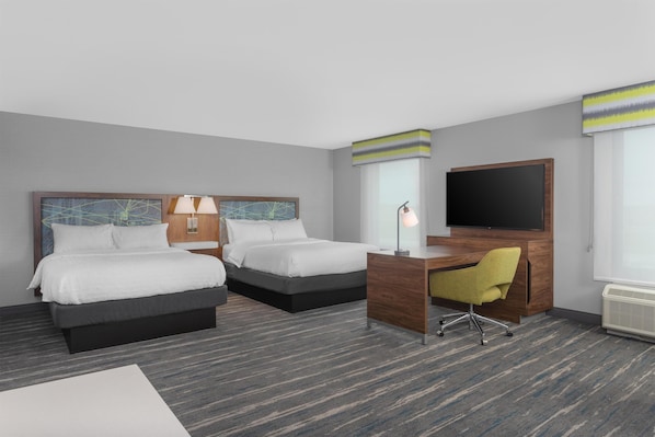 Habitación de hotel con dos camas, un escritorio, una silla, un televisor y una ventana con persianas.