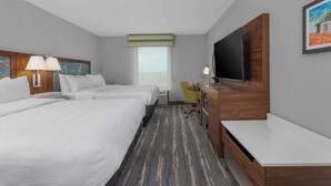 Ein Hotelzimmer mit zwei Betten, einem Schreibtisch, einem Fernseher und einem Fenster.