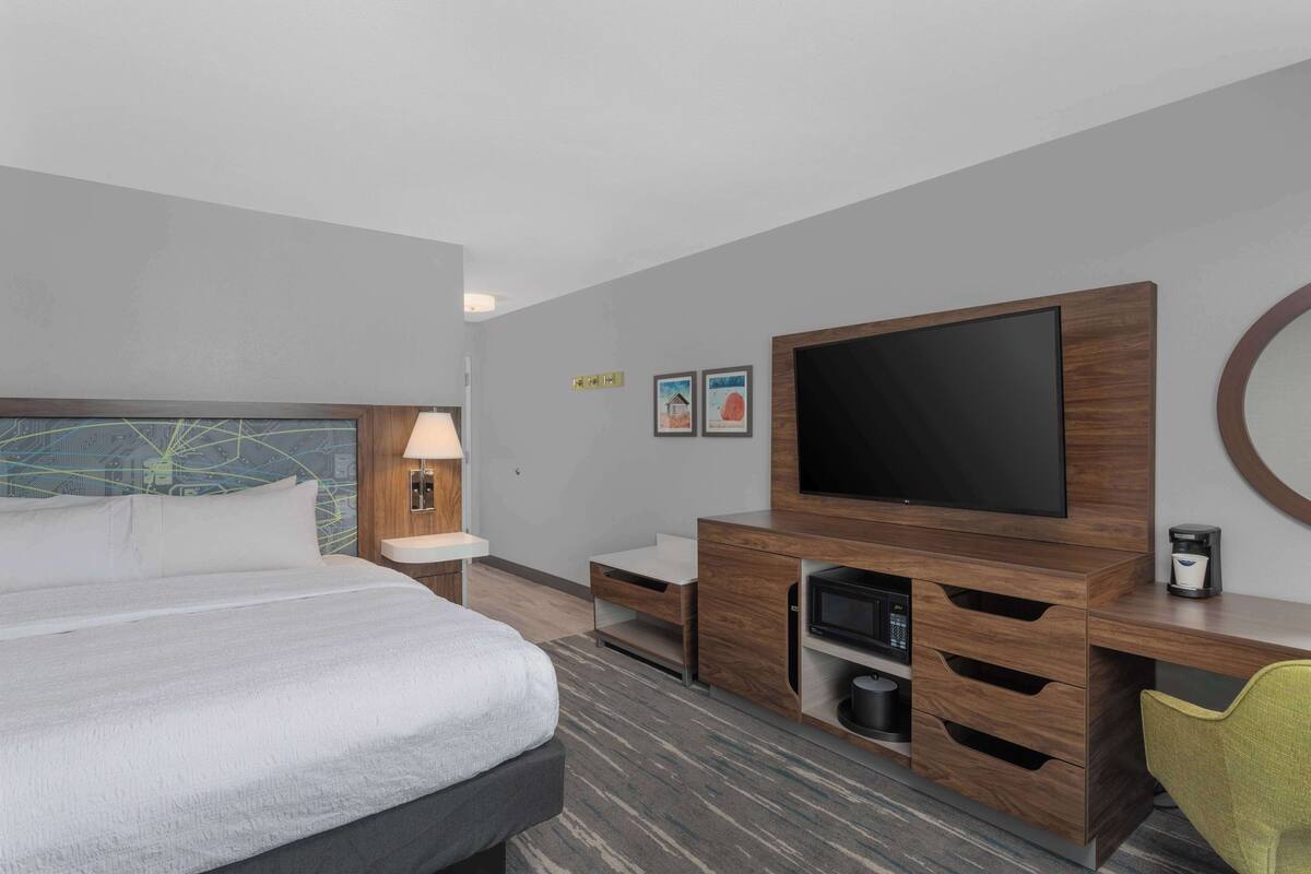 A hotel room with a bed, a TV, a desk, and a chair.