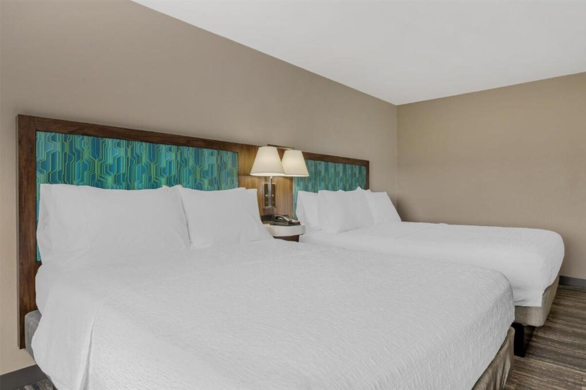 Ein Hotelzimmer mit zwei Betten, einem geometrisch gemusterten Kopfteil, einer Nachttischlampe und einem Holzboden.