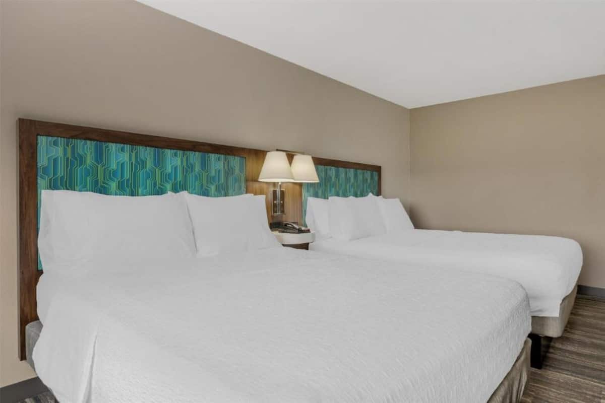 A hotel room with two beds, a headboard with a geometric pattern, a bedside lamp, and a wooden floor.