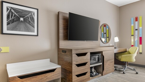 A hotel room with a wooden desk, a flat-screen TV, a mirror, and a colorful abstract art piece on the wall. - Hampton Inn & Suites Crawfordsville (Crawfordsville)