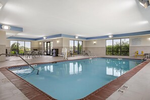 Una piscina interior con agua cristalina, rodeada por una terraza con baldosas y un borde de ladrillo.