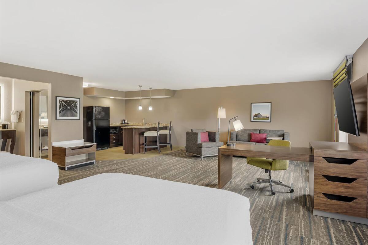 A hotel room with a bed, desk, and kitchenette.