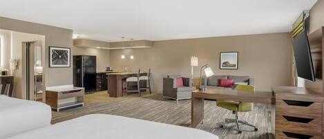 A hotel room with a bed, desk, and kitchenette.