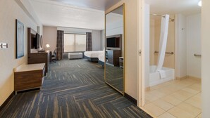 A hotel room with a large bed, a desk, a mirror, a TV, a shower, and a carpeted floor. - Hampton Inn & Suites Plattsburgh (Plattsburgh)