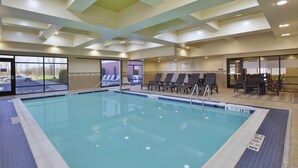 An indoor swimming pool with clear blue water, lounge chairs, and a tiled floor.