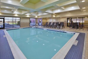 An indoor swimming pool with clear blue water, lounge chairs, and a tiled floor.