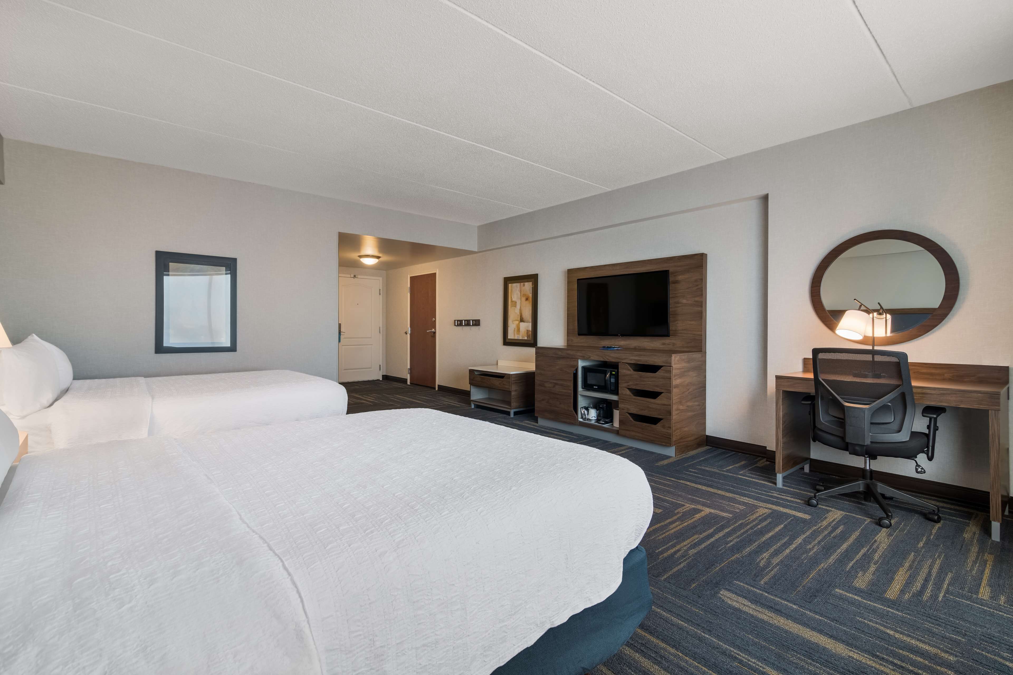 Una habitación de hotel con una cama grande, un escritorio con una silla, un televisor y un espejo.
