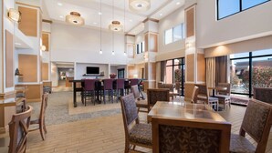 A spacious hotel lobby with a central bar area, multiple seating arrangements, and large windows offering views of the outdoors. - Hampton Inn & Suites Plattsburgh (Plattsburgh)