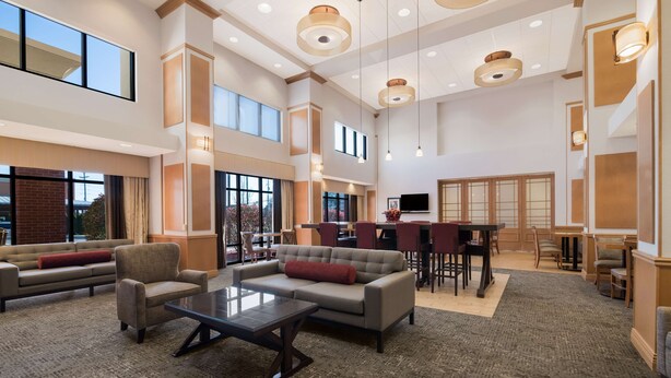 A spacious lobby with a high ceiling, large windows, and a seating area with sofas and a coffee table. - Hampton Inn & Suites Plattsburgh (Plattsburgh)