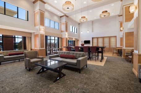 A spacious lobby with a high ceiling, large windows, and a seating area with sofas and a coffee table.
