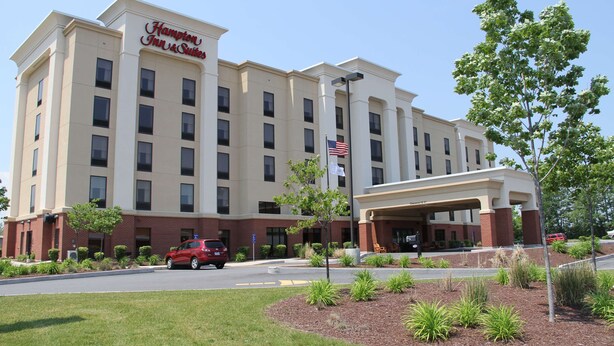 A Hampton Inn & Suites hotel with a large entrance, a flag, and a red car parked in front.
