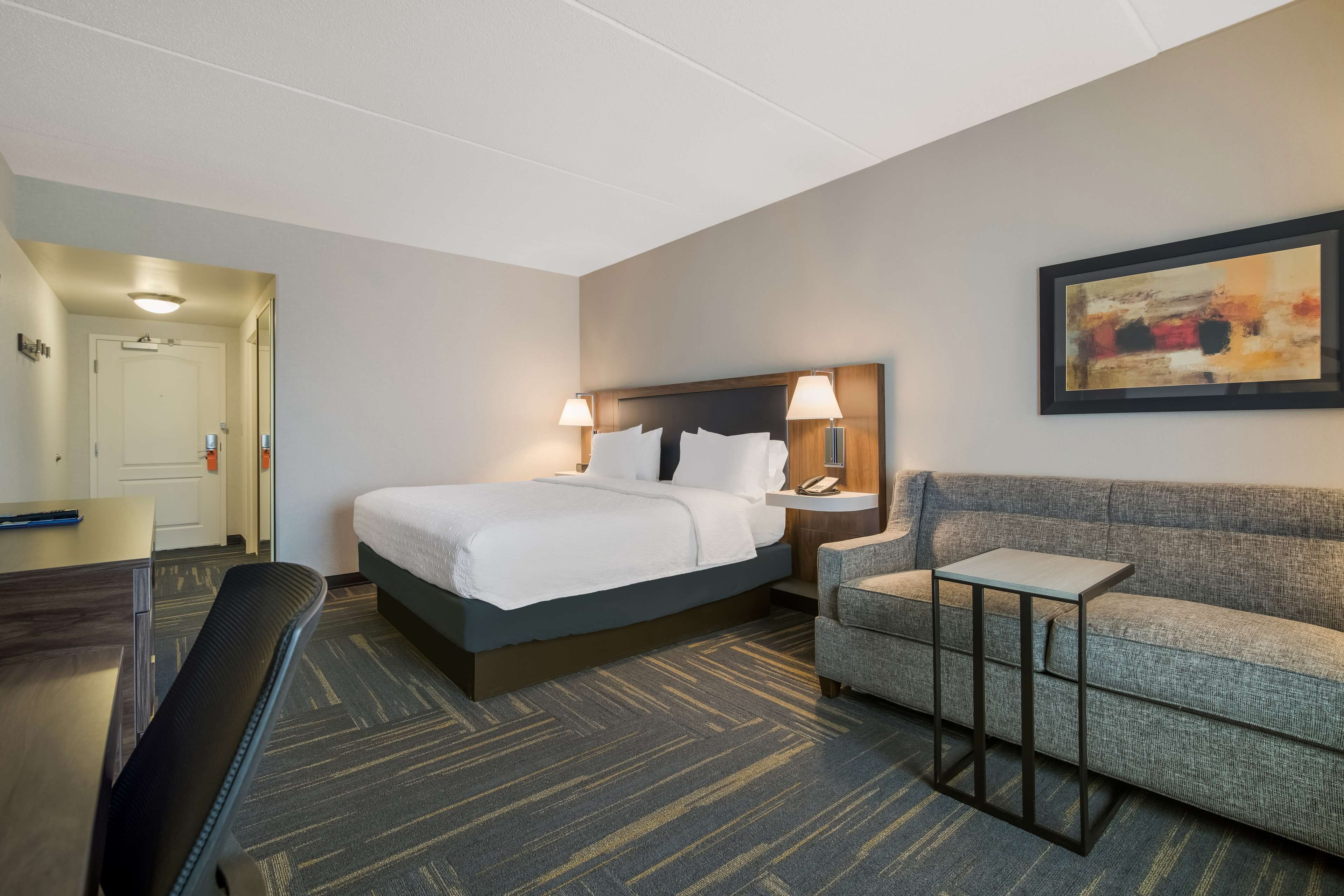 A hotel room with a bed, a desk, a chair, a sofa, and a small table.
