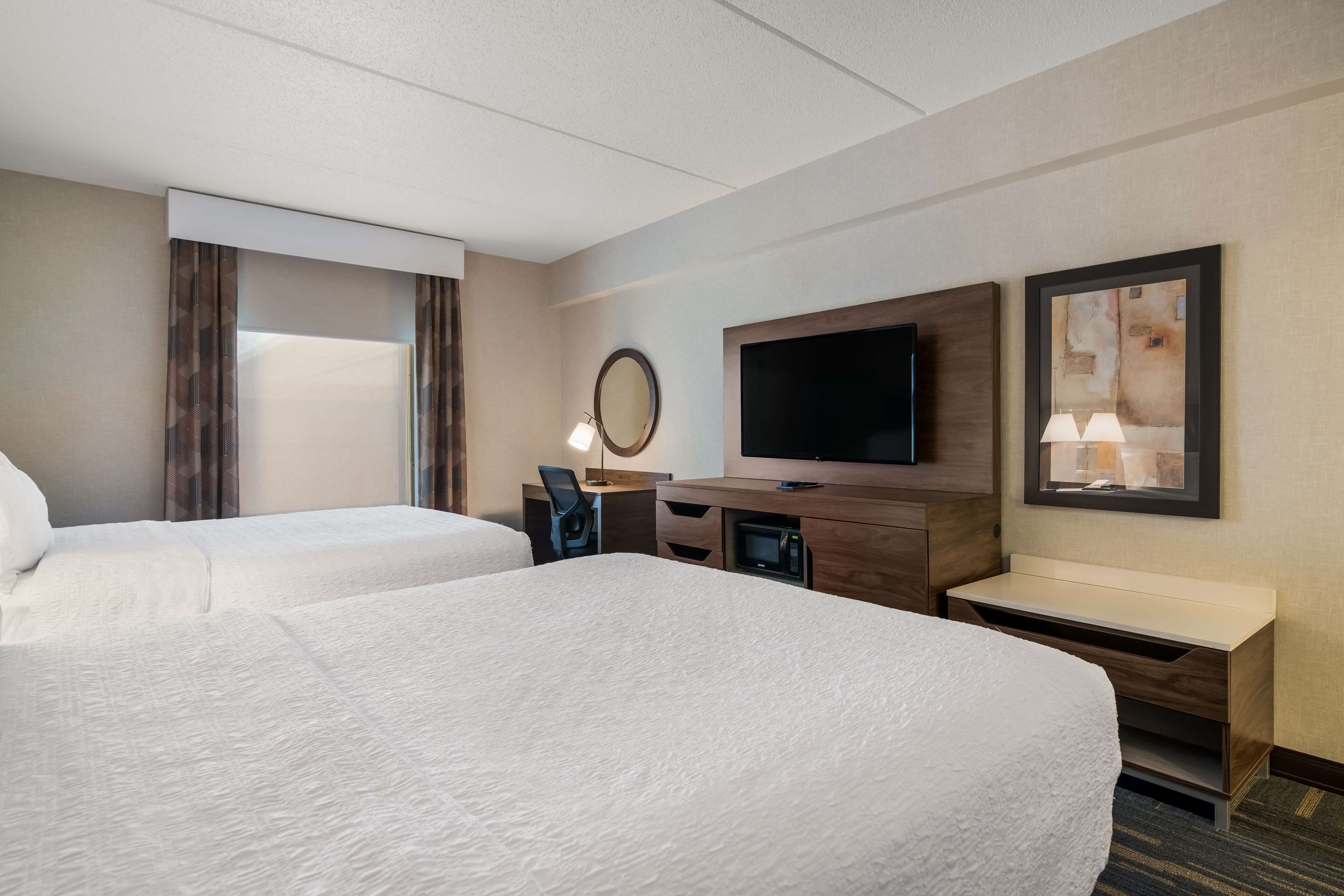 A hotel room with two beds, a desk, a TV, and a painting on the wall.