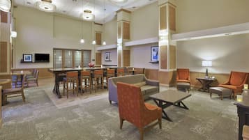 Un hall de hotel con zona de bar, arreglos de asientos y un televisor.