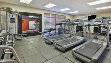 A gym with treadmills, weight machines, and a wall-mounted TV.