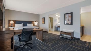 A hotel room with a bed, desk, chair, and a bathroom with a sink and mirror.