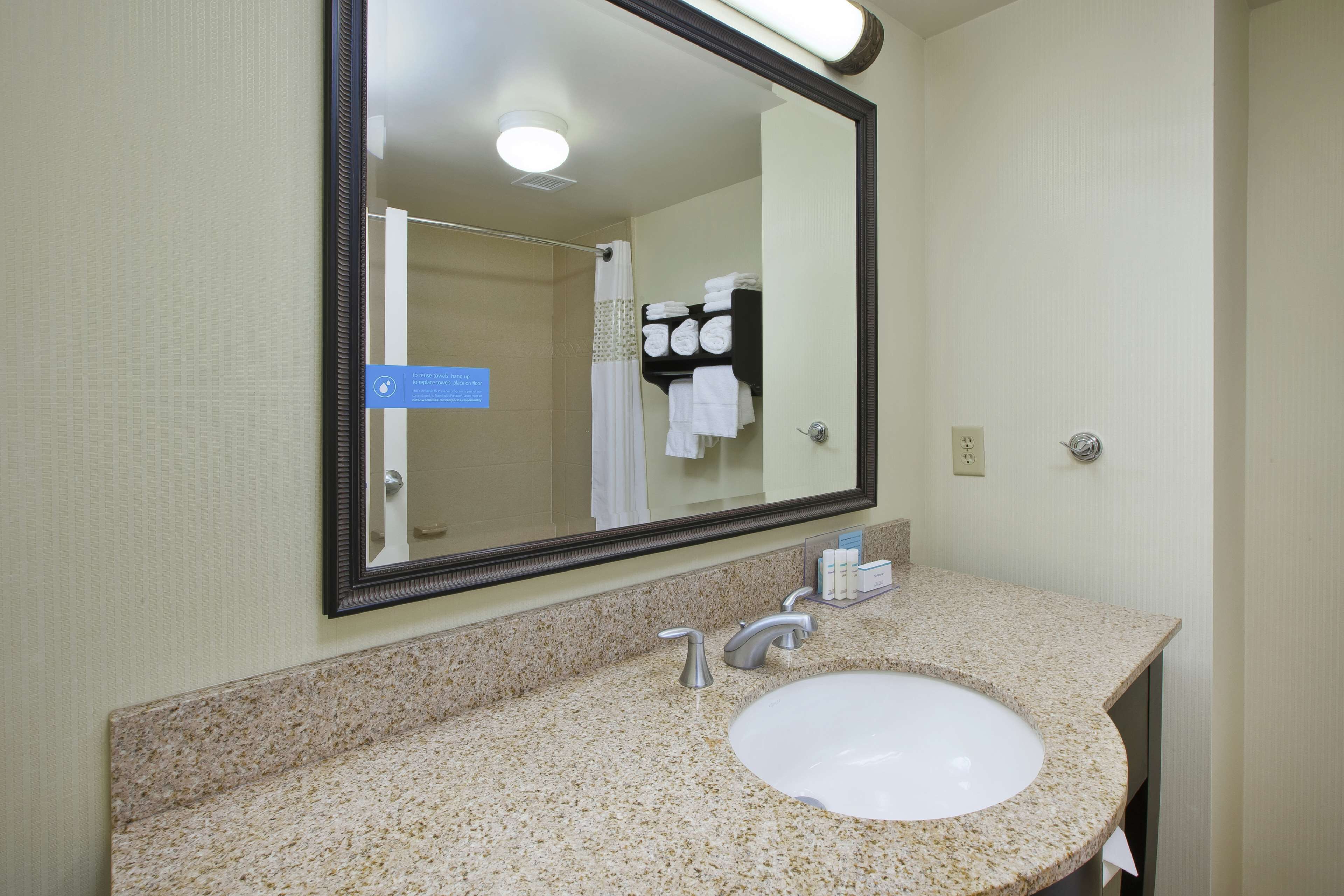 A bathroom with a granite countertop, a white sink, a large mirror, and a towel rack with folded towels.
