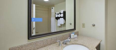 A bathroom with a granite countertop, a white sink, a large mirror, and a towel rack with folded towels.