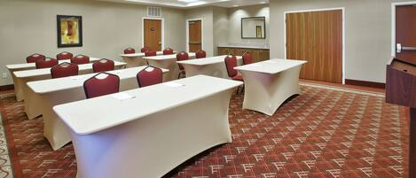 A conference room with tables and chairs, a large mirror, and a patterned carpet.