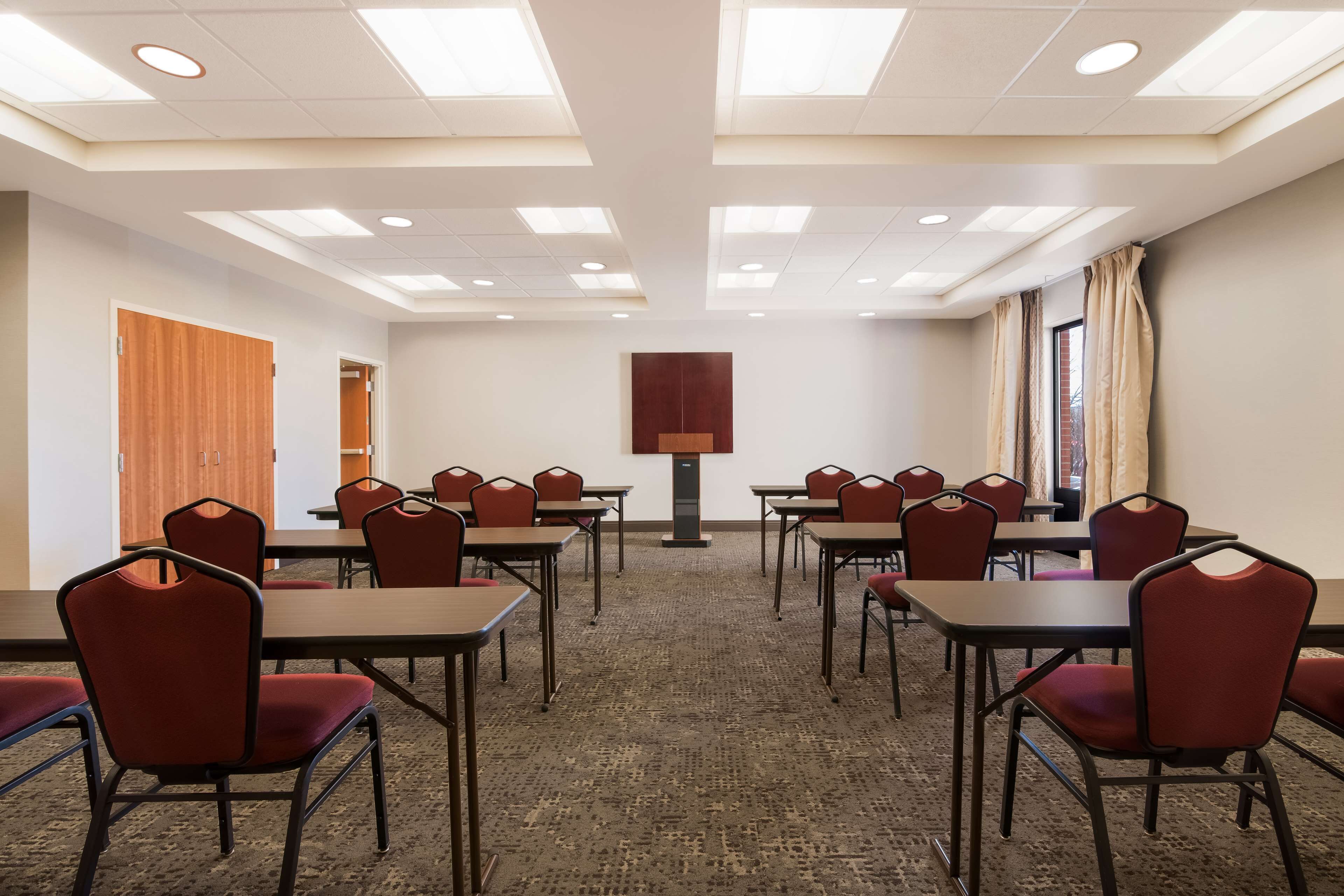 Una sala de conferències amb diverses taules i cadires, un terra amb moqueta i un sostre amb il·luminació empotrada.